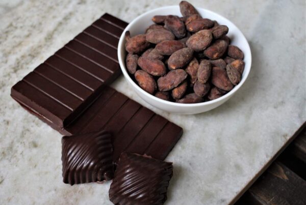 Homemade bean-to-bar dark chocolate bars with whole cacao beans on marble slab