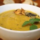 Pumpkin soup in a ceramic bowl, garnished with fresh basil leaves